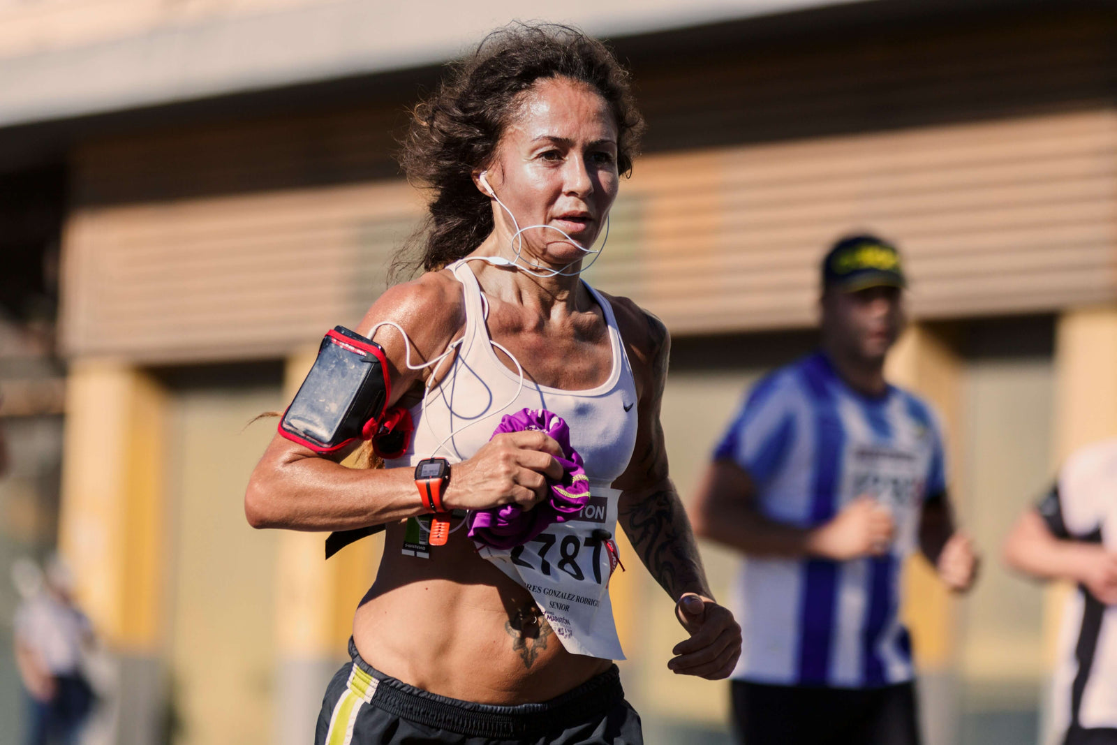 Female running with a smartphone strapped to her arm; wearing headphones and a white Nike running top.