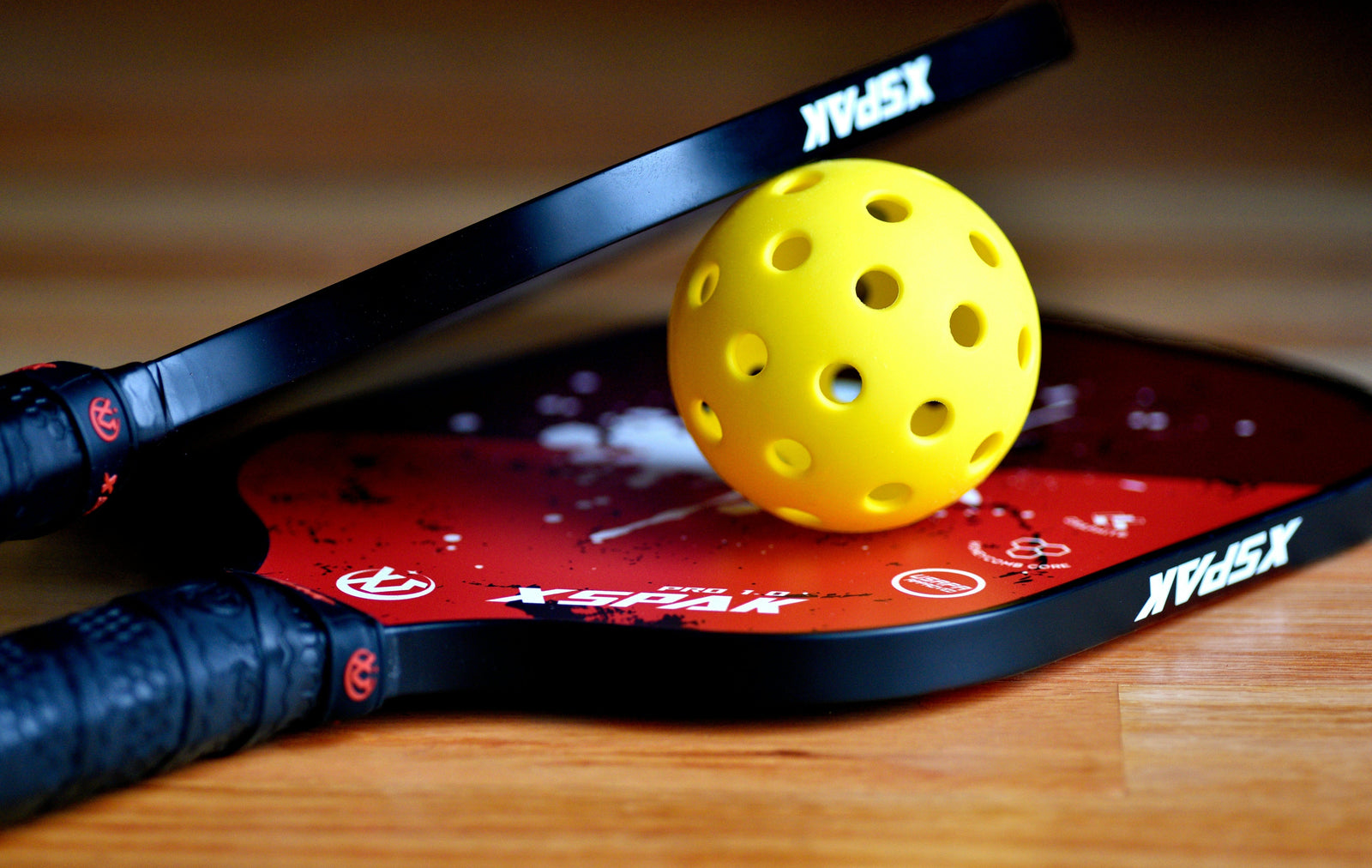 A yellow ball in between two identical padel rackets