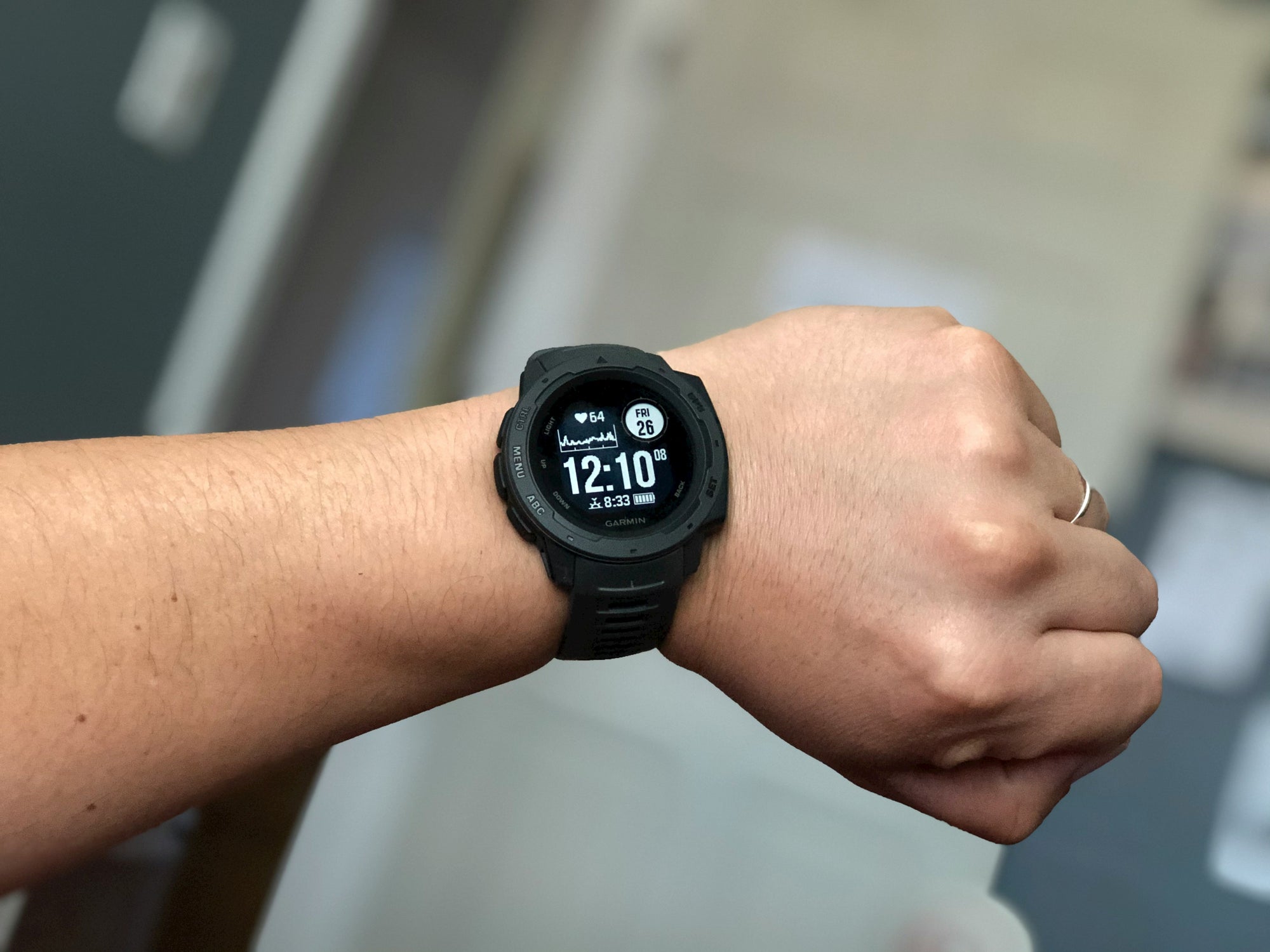 A males wrist wearing a black Garmin GPS running and hiking watch displaying the time, date, and other fitness tracking information on the screen.