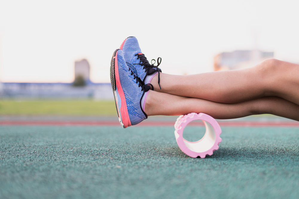 An athlete resting both legs on a foam roller, on a track