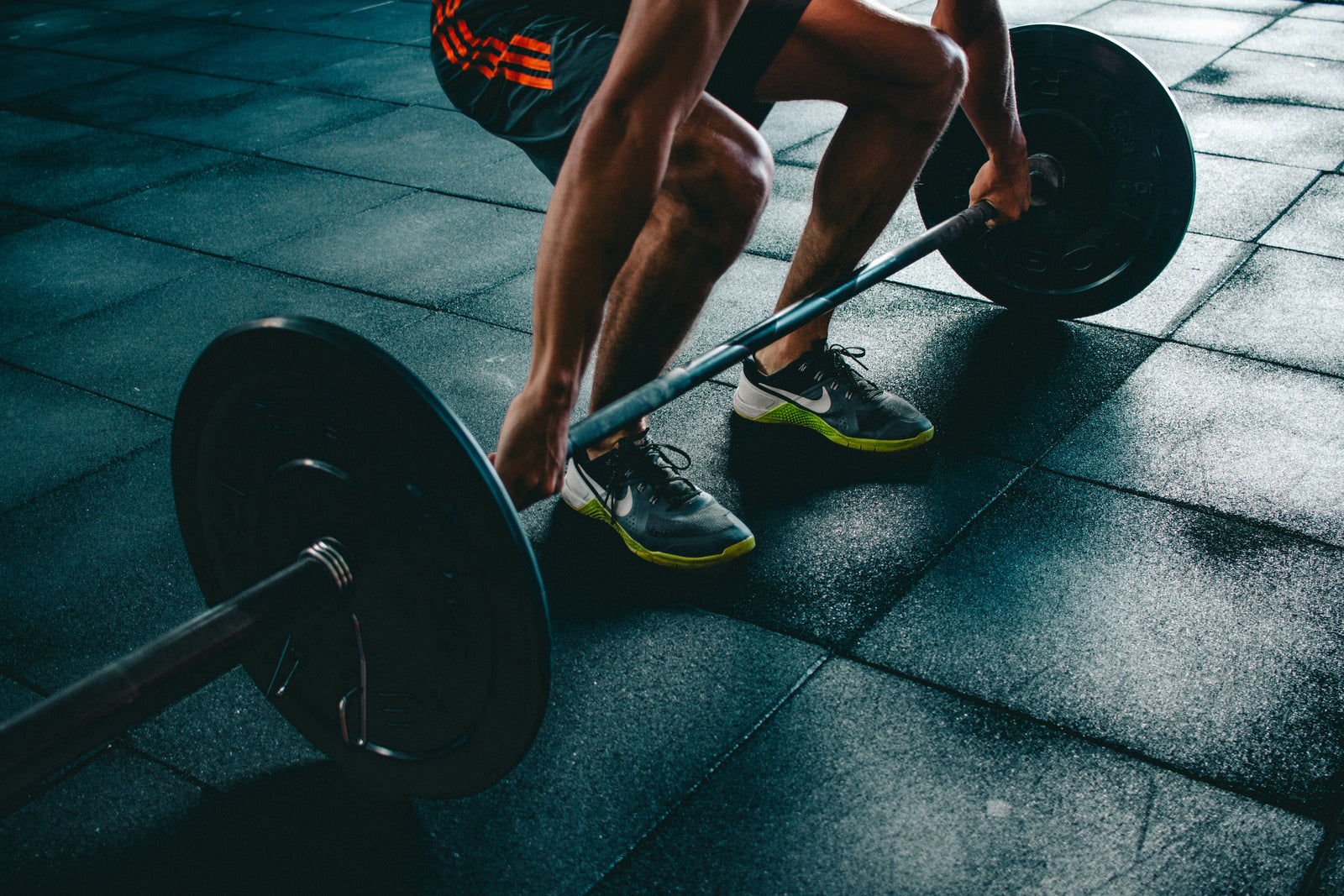 A person performing a deadlift exercise at the gym, wearing training shoes with vibrant yellow accents on the soles