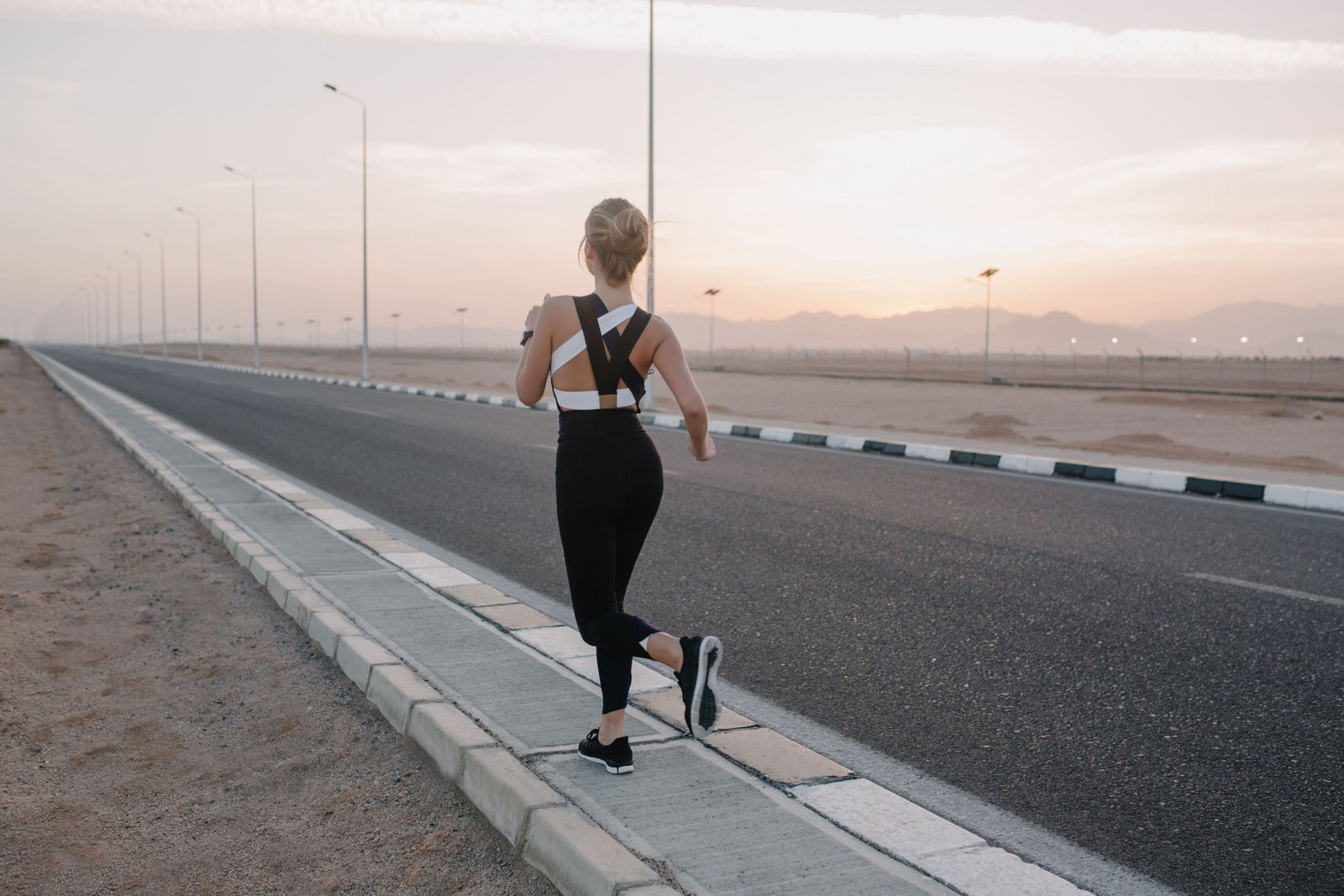 A young woman running in black and white athleisure, with matching road running shoes