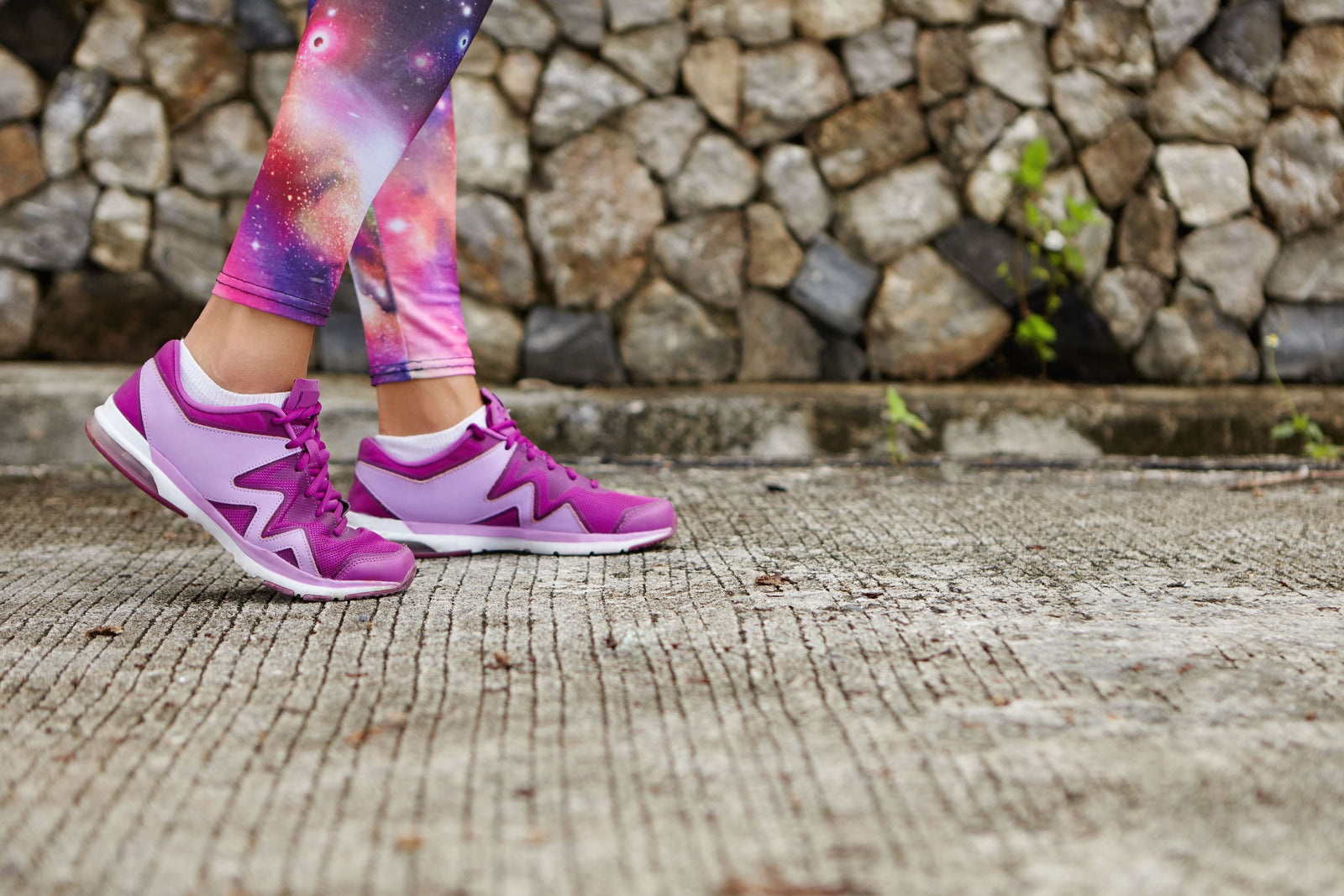 A female runner wearing bright, must-have ladies running shoes in purple and matching tights, running on a road