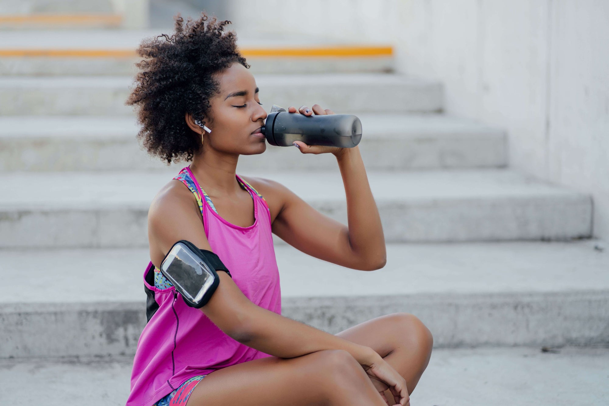 Female athlete practising runner’s hydration strategies while resting on a step 