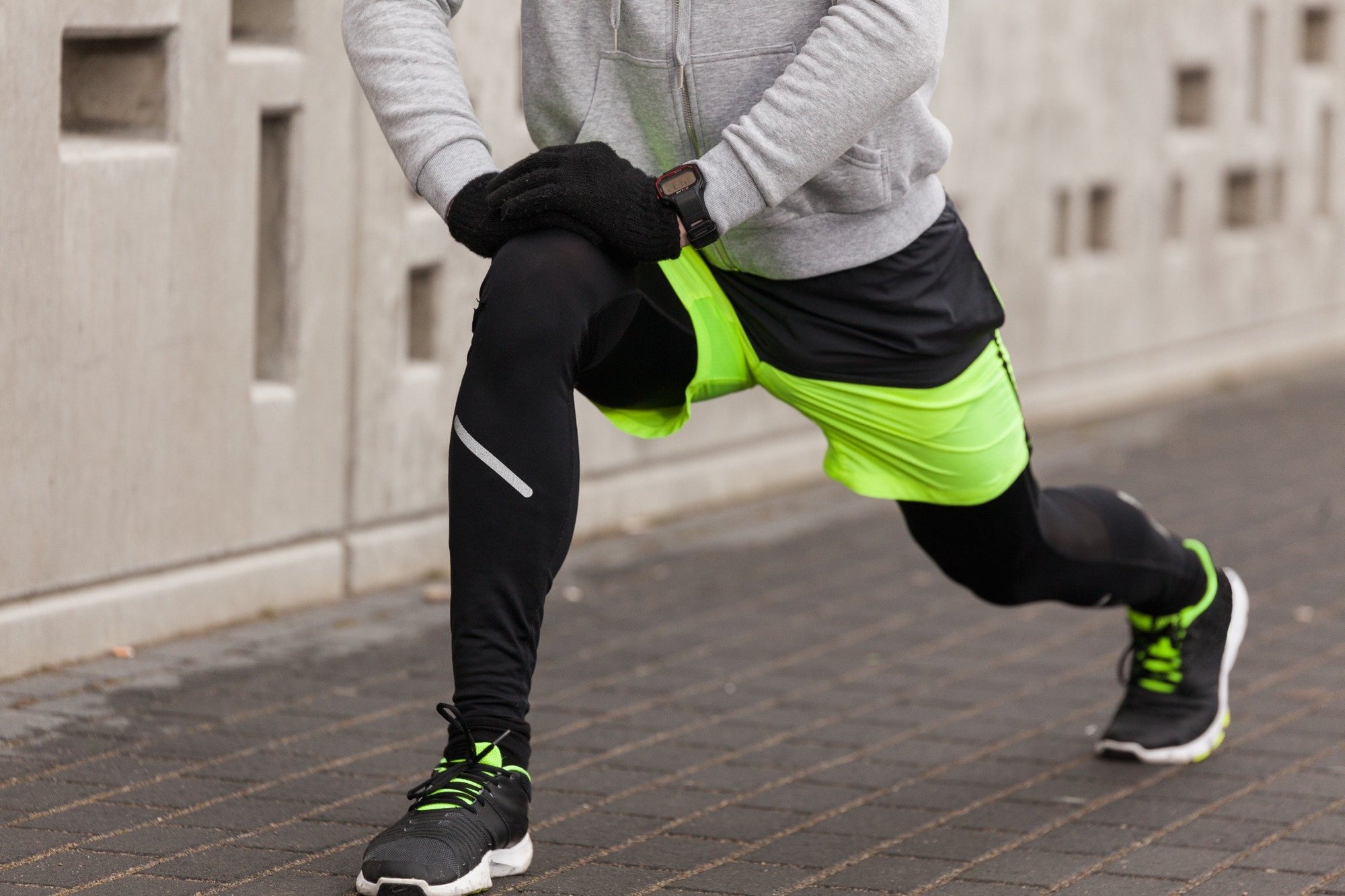 Runner stretching in neon green shorts and black leggings before a run