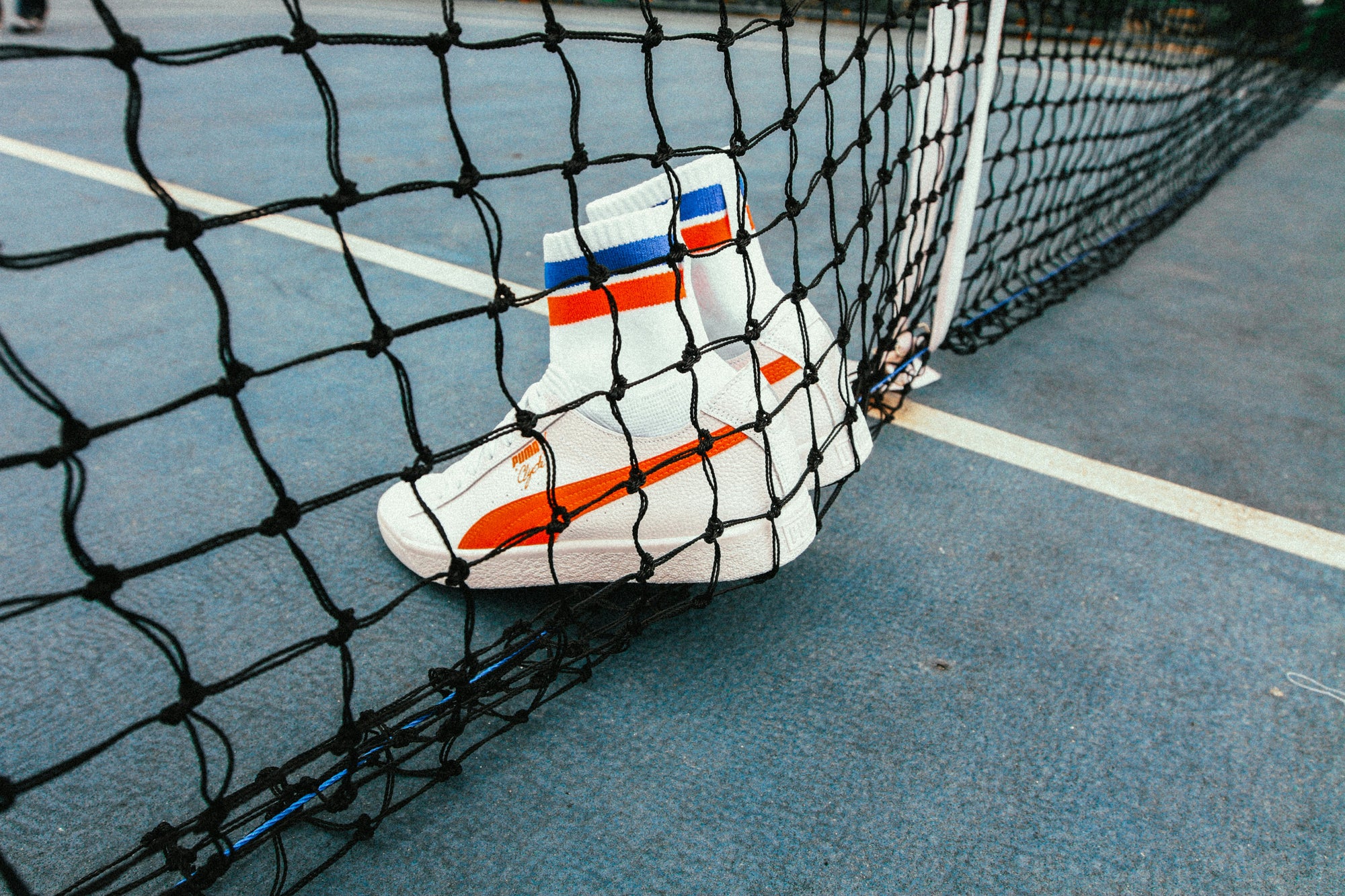 White and Orange puma shoes on a tennis net