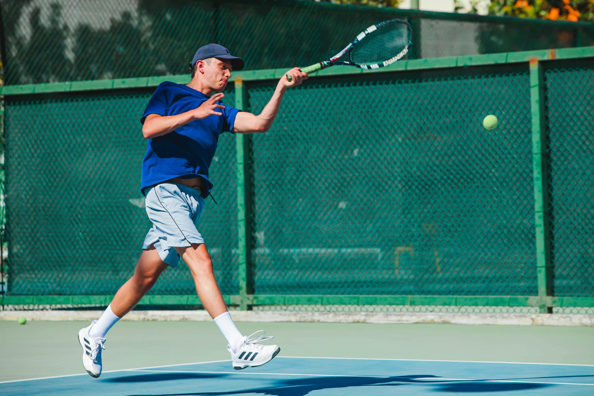 Man wearing a blue cap and shirt playing tennis in strong men's tennis shoes