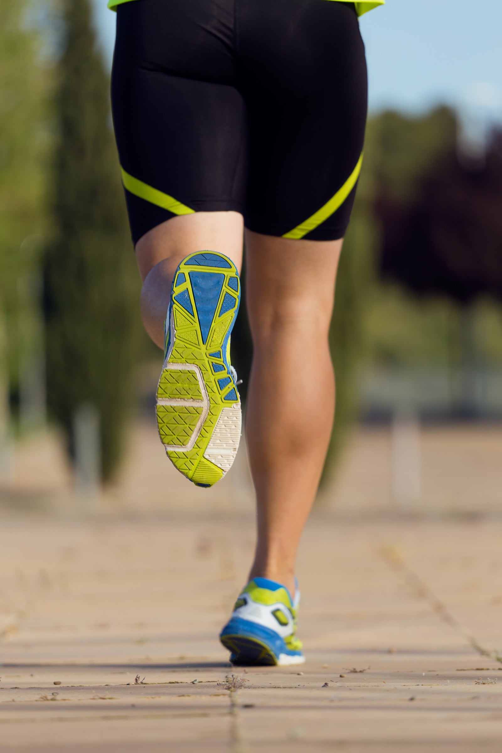 A road runner in a running motion, wearing a pair of neon, blue and white minimalist running shoes