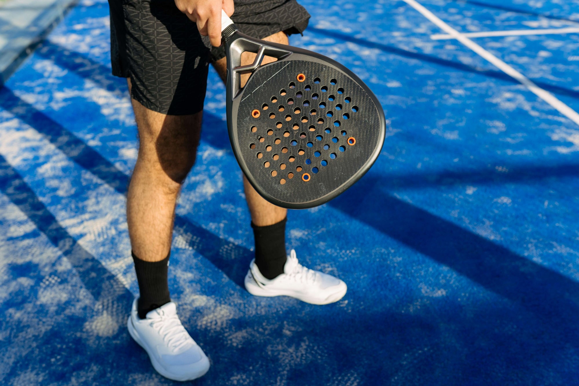 Male player standing on a Padel court holding a racket and wearing the best Padel shoes