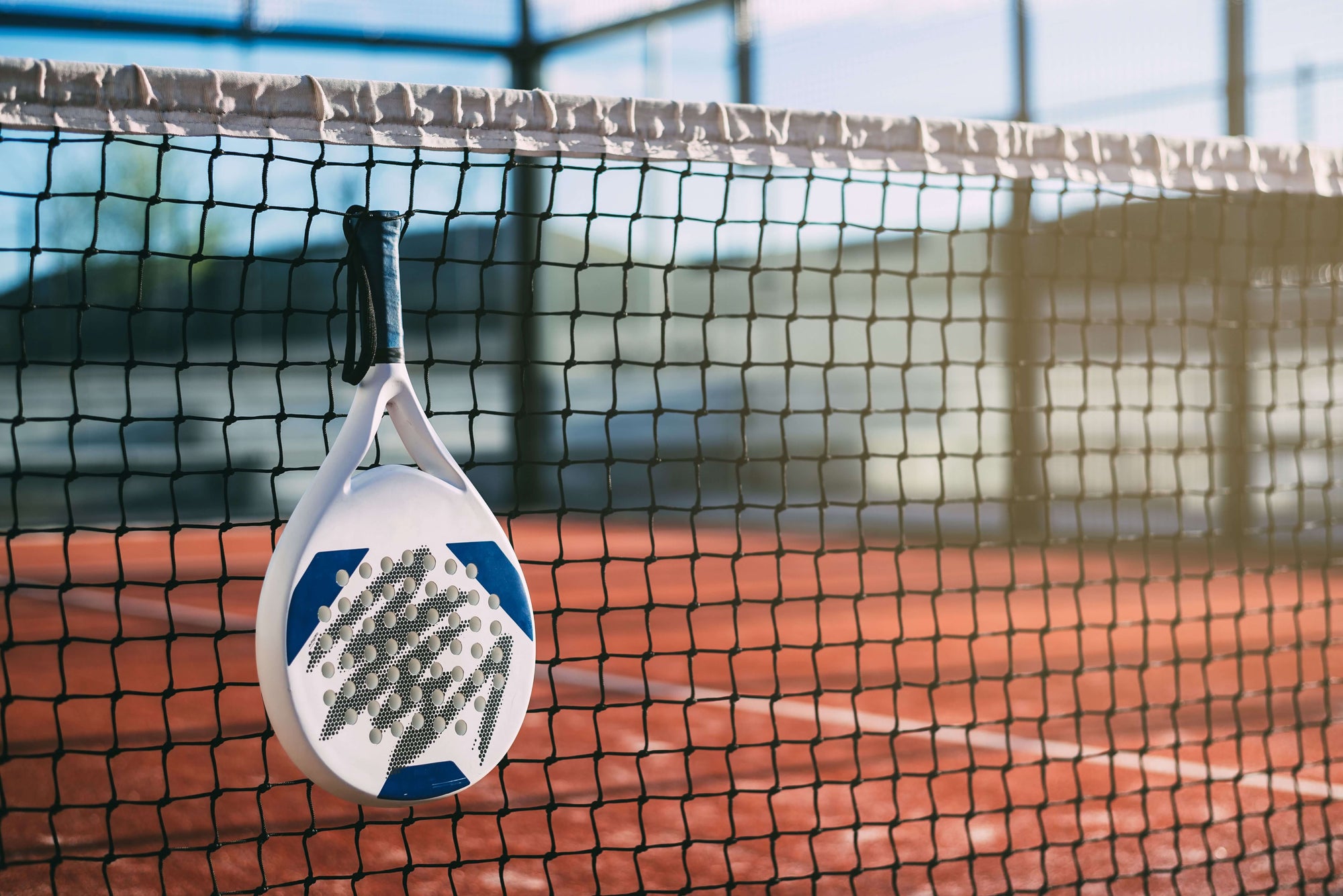 A quality Padel racket hanging on the net of a Padel court as part of the ultimate Padel Gear