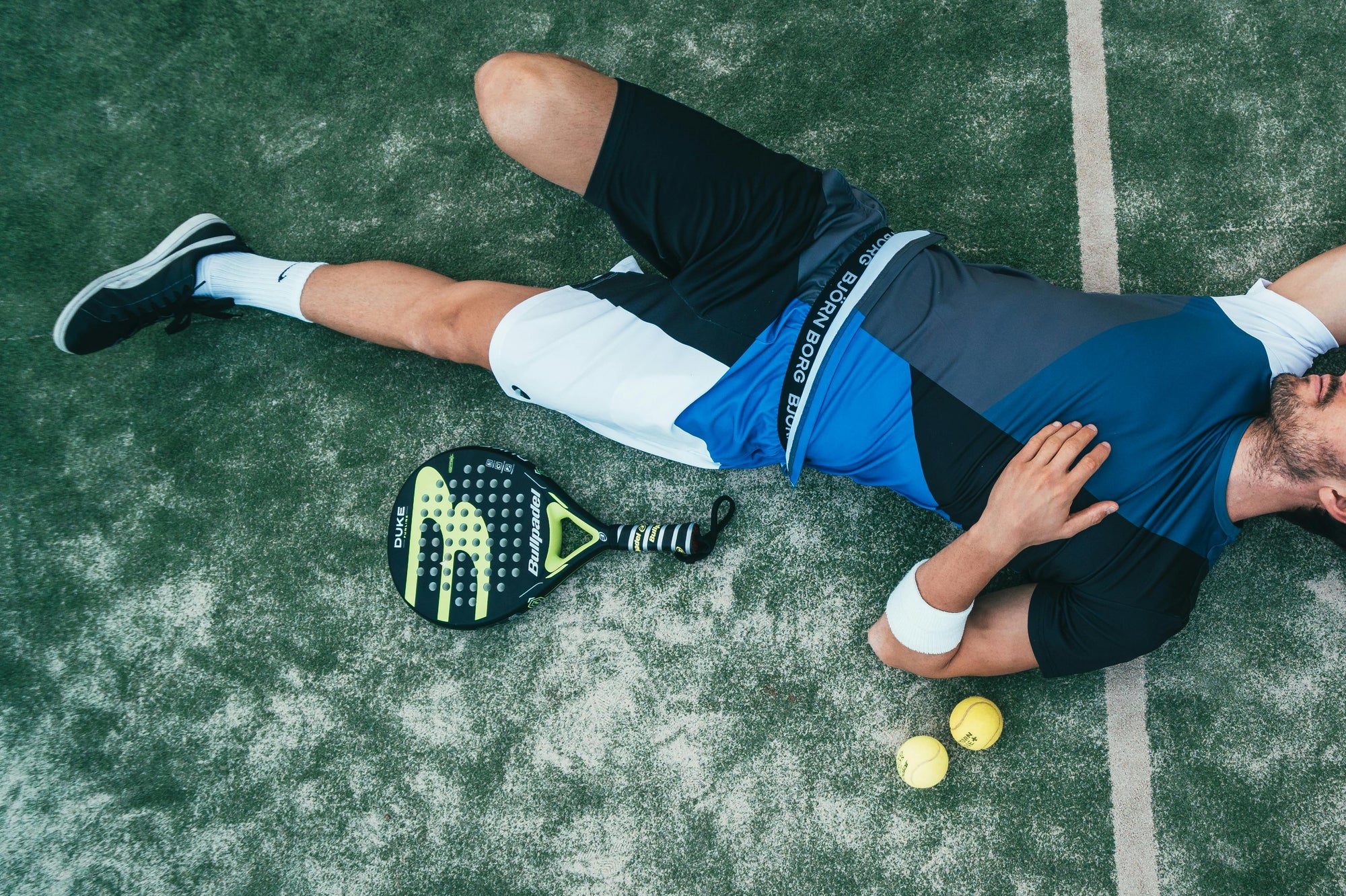 A man in padel gear laying on padel court