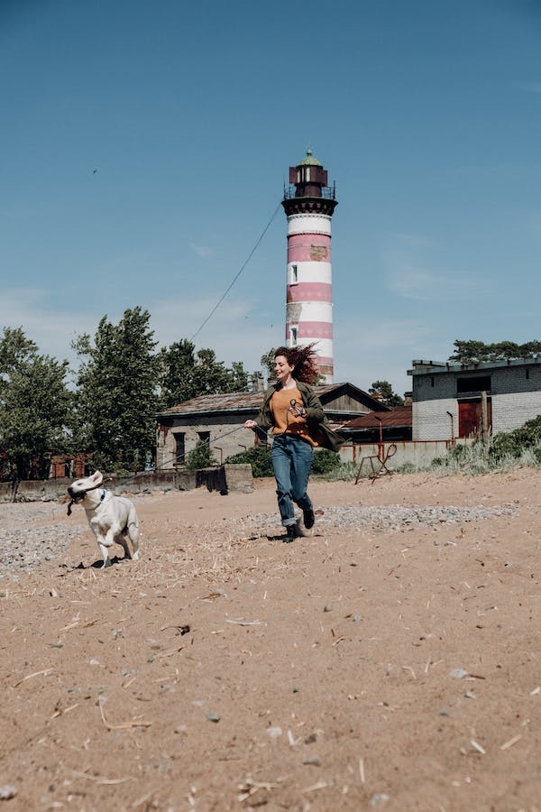 A woman running with her dog on a leash near a lighthouse on sunny day