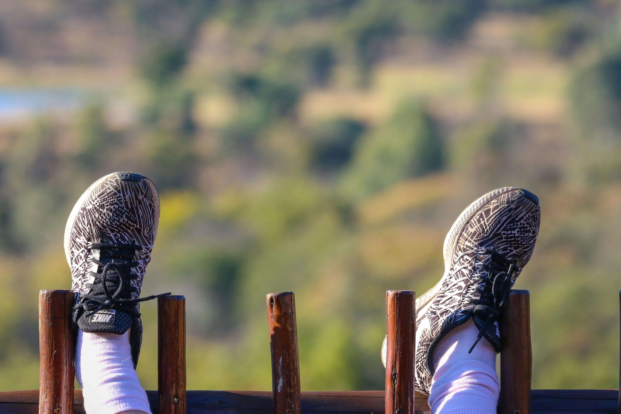 Runner resting wearing trail running shoes and resting their feet on a wooden fence