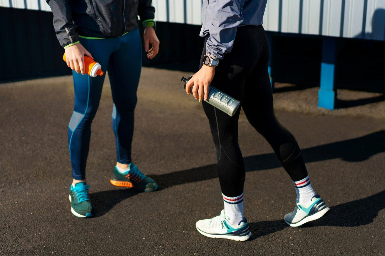 Two people in layered running pants with water bottles outdoors.