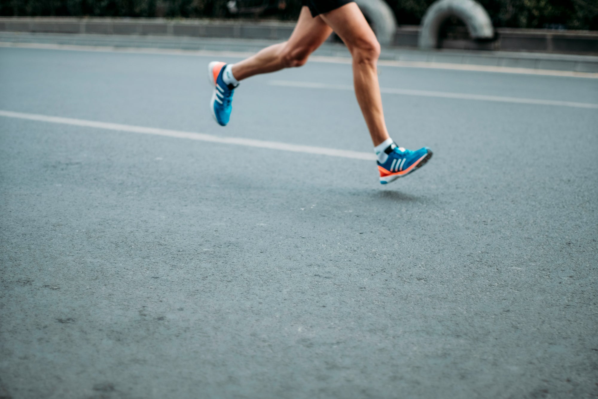 Runner wearing blue shoes and white support socks mid-stride on a road