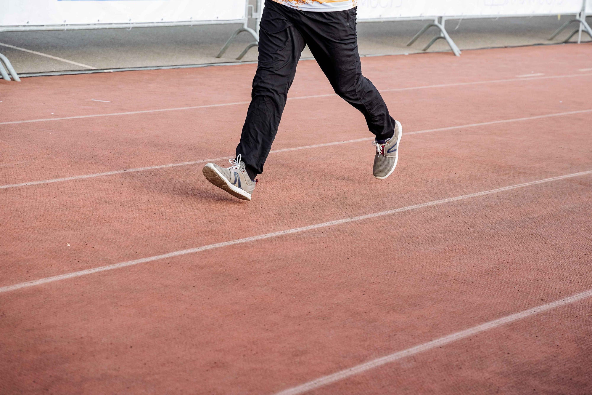 a man running on a track wearing black running pants and grey shoes.