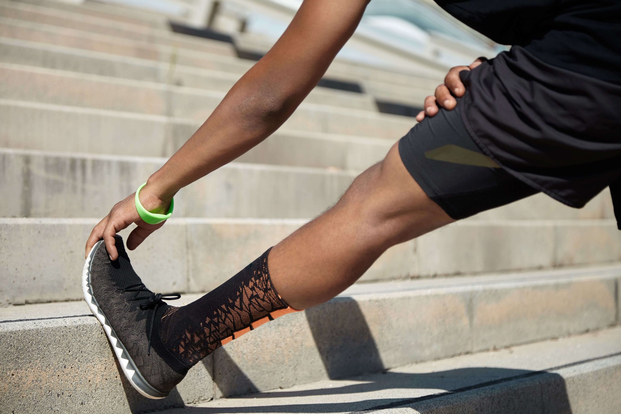 Young male athlete wearing a pair of black and orange anti-blister socks, stretching on stairs